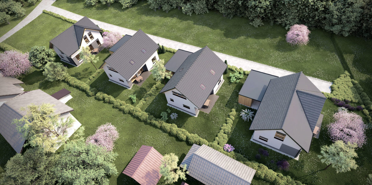 Zračni pogled na manjše stanovanjsko naselje enodružinskih hiš z dvokapnimi strehami, urejenimi vrtovi, zelenimi površinami in mirno bivalno okolico.